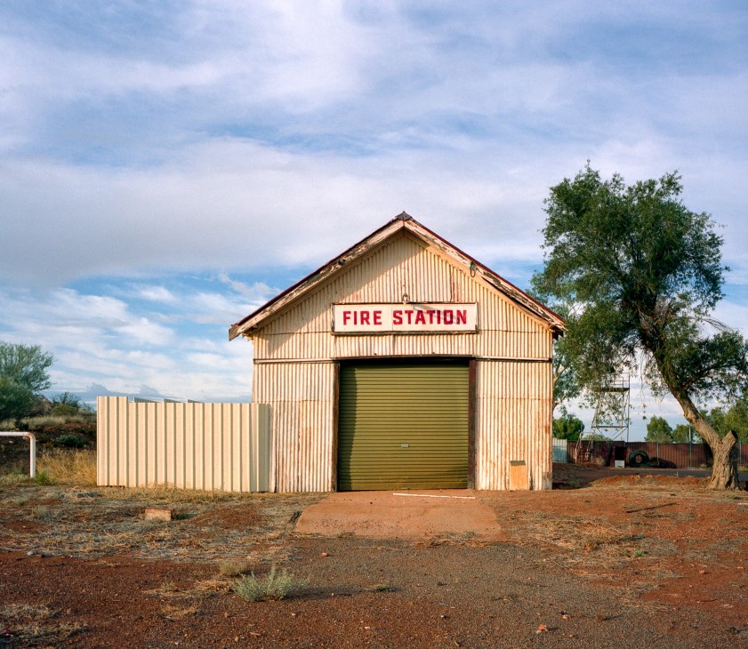 A corrugated metal fire station building with red lettering under blue sky in rural Australia.