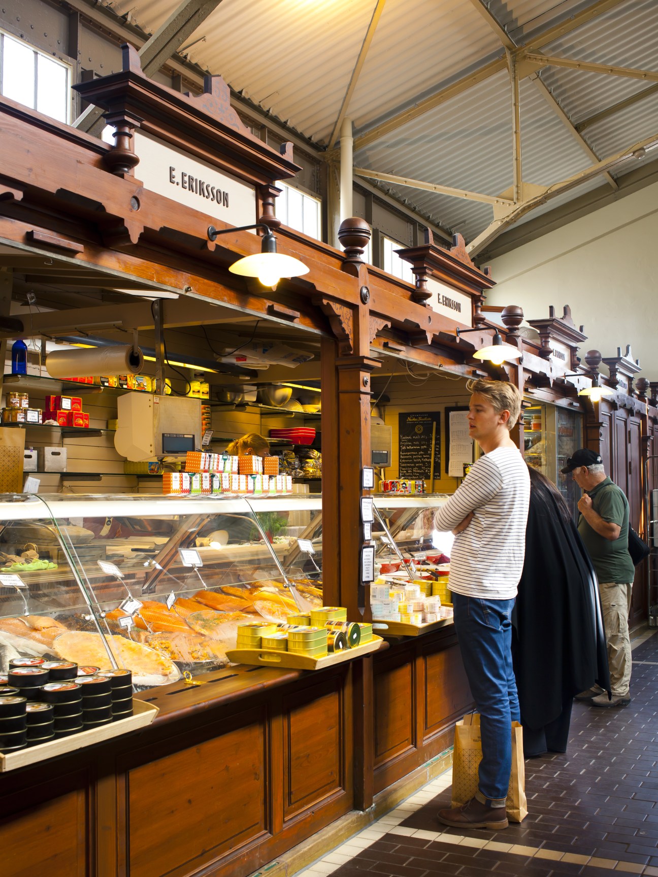 Customer browsing fresh fish and seafood at E Eriksson fishmonger counter in Helsinki market.
