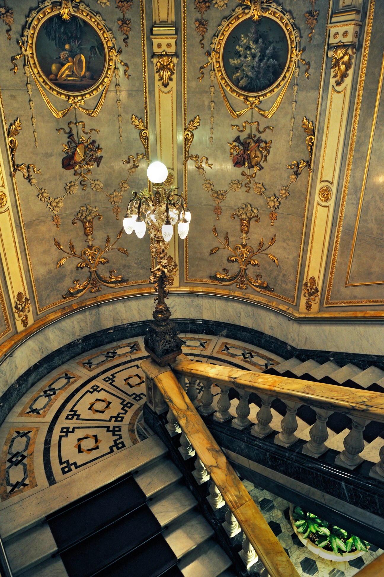 Ornate ceiling with gold leaf details and chandelier above a spiral staircase at San José's National Theatre.