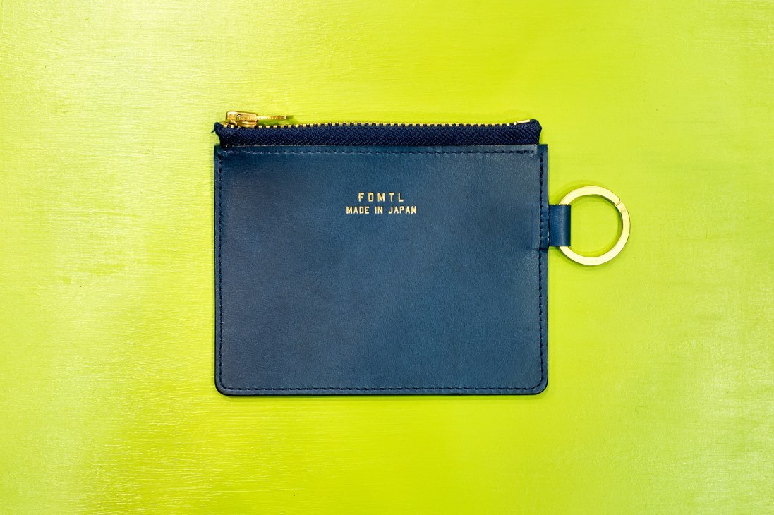 Navy leather card holder by Fundamental Agreement Luxury with gold zipper on bright yellow background.