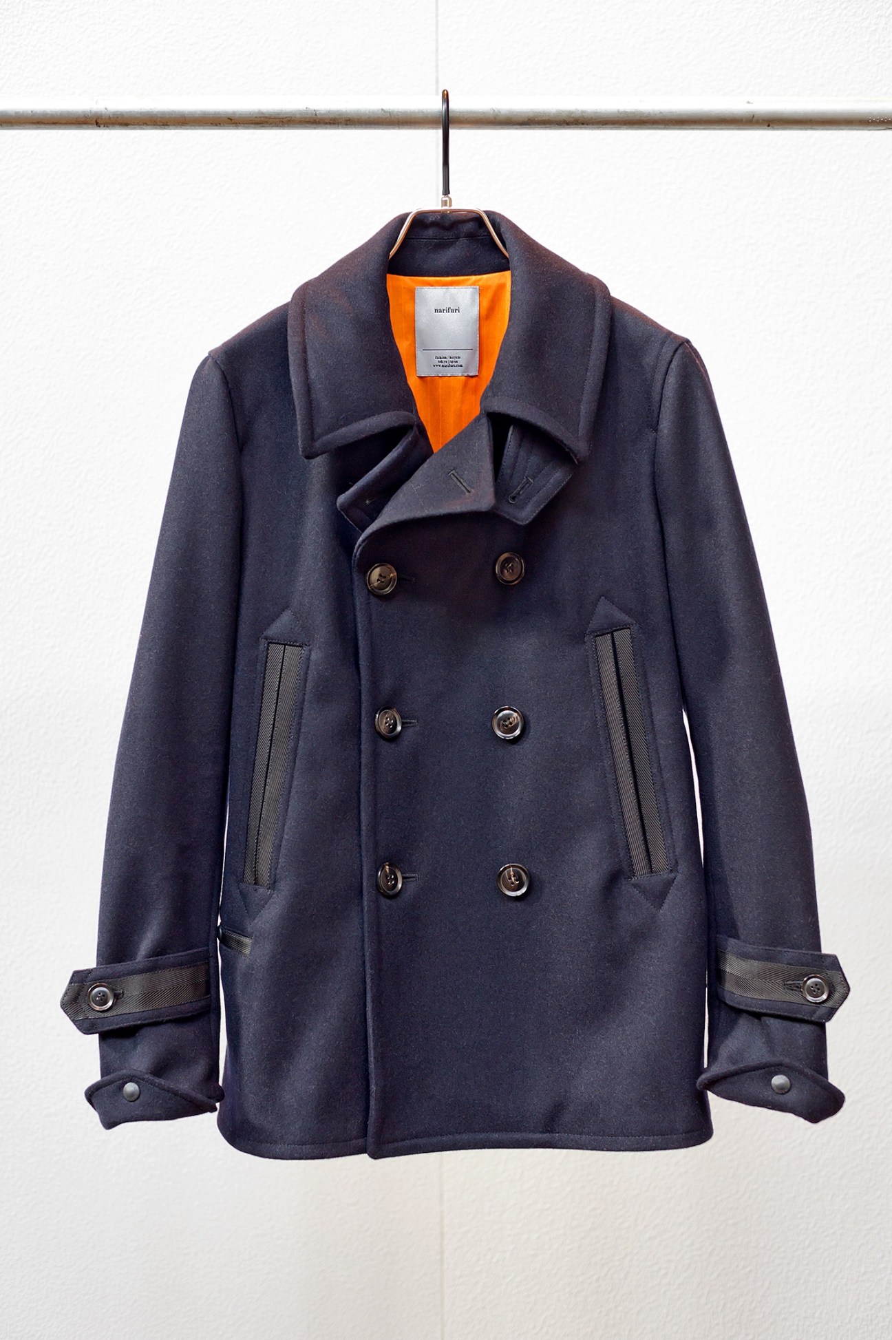 Navy double-breasted jacket by Narifuri with orange lining, hanging on a rail.