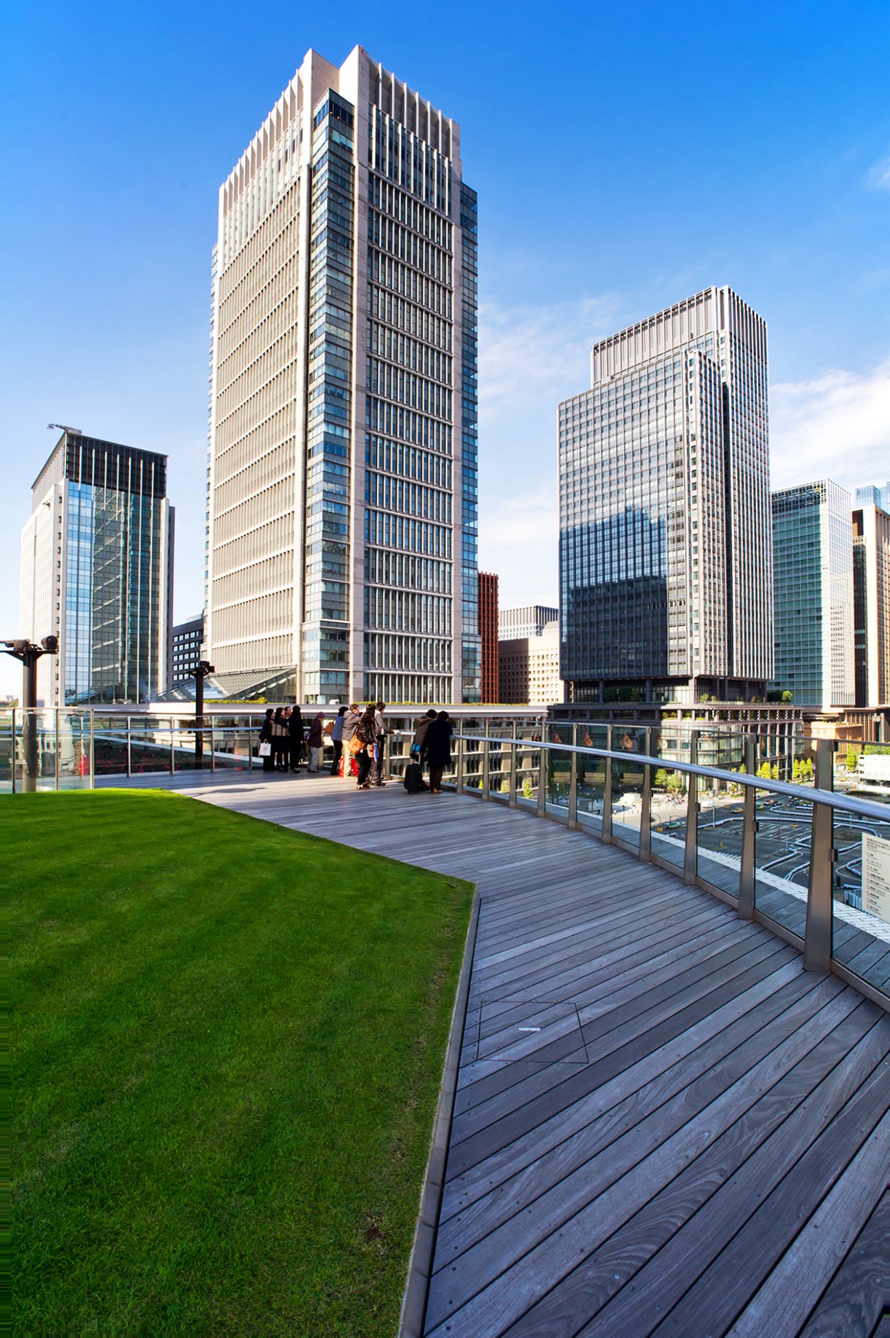 Modern Tokyo office towers with retail spaces viewed from a terrace with green lawn and wooden deck