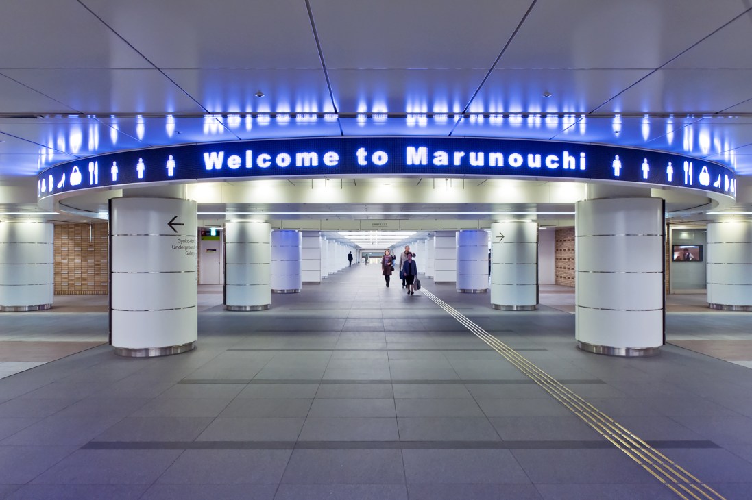 Underground gallery with blue-lit 'Welcome to Marunouchi' sign and modern minimalist architecture.
