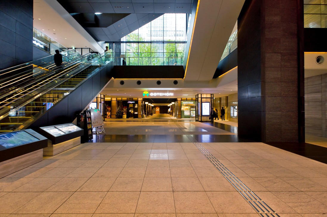 Modern interior of Otemachi Tower showing escalators, retail storefronts, and natural light from skylights.