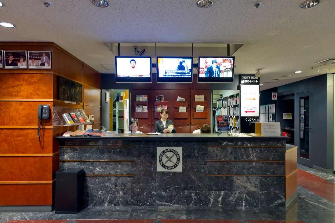 Front desk of Foreign Correspondents' Club of Japan with staff, monitors, and wooden cabinetry displaying the FCCJ logo.