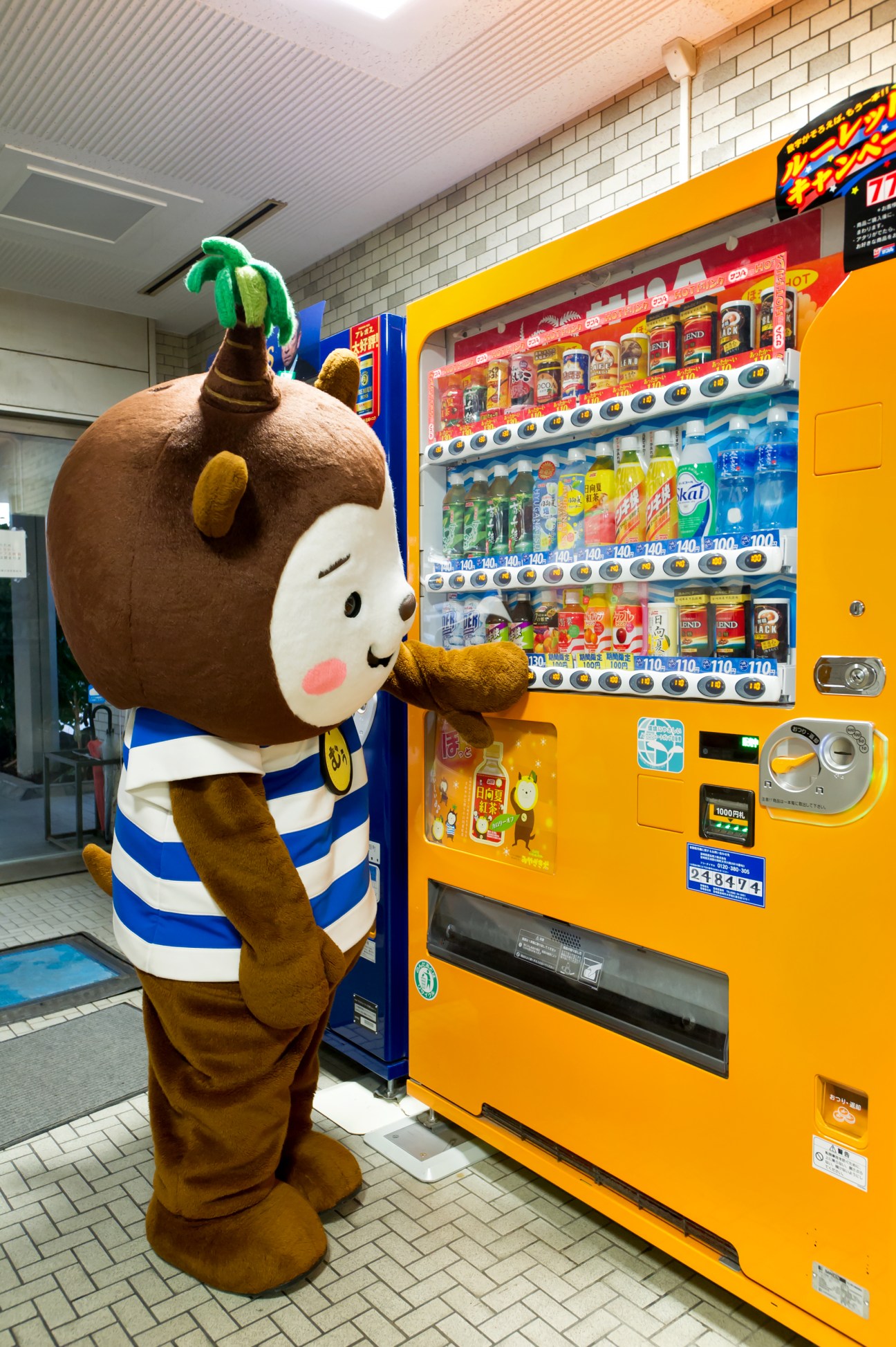 Muu-chan mascot character posing beside a yellow vending machine in Japan.
