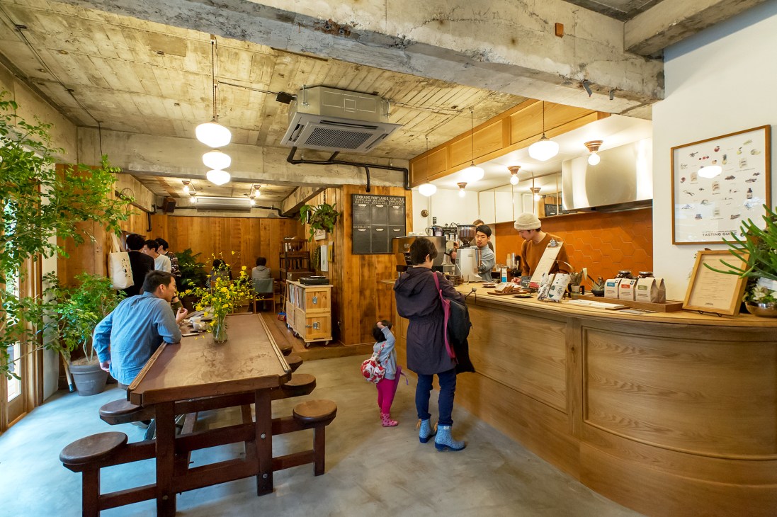 Interior of Paddlers Coffee in Tokyo showing wooden counter, customers, pendant lights, and plants.