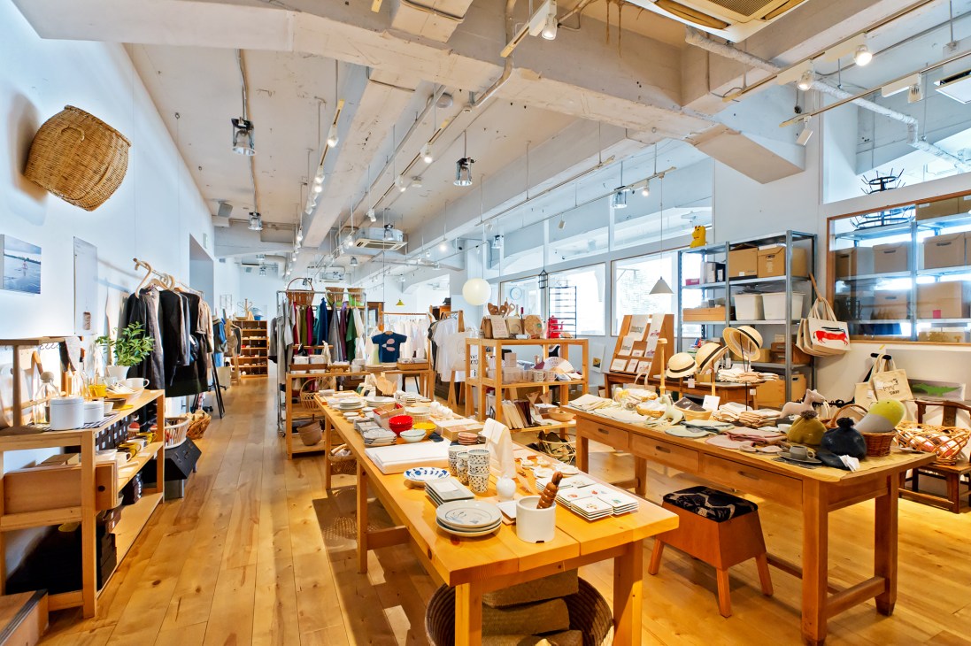 Interior of Claska Gallery & Shop Do homeware store with wooden display tables, clothing racks, and ceramic items under industrial ceiling lights.