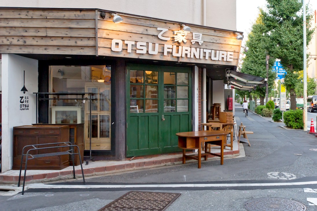 Otsu Furniture storefront on a Tokyo street with wooden signage, green doors, and vintage furniture displayed outside.