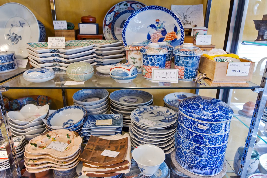 Display shelf of Japanese ceramics including blue and white plates, bowls, and decorative containers with price tags.