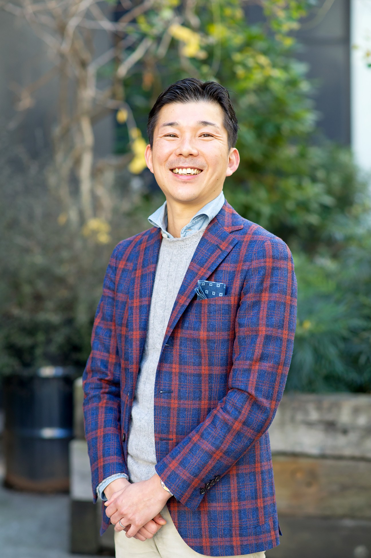 Kentaro Harada, assistant manager of Beams' human-development department, smiling outdoors in a red and blue plaid blazer.