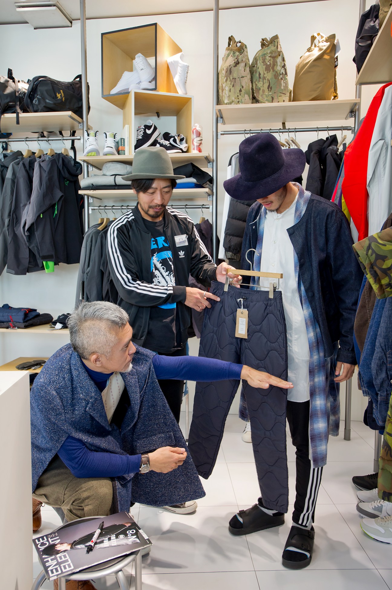 Kenjiro Wada demonstrates styling advice to Beams staff in a shop with clothing displays.