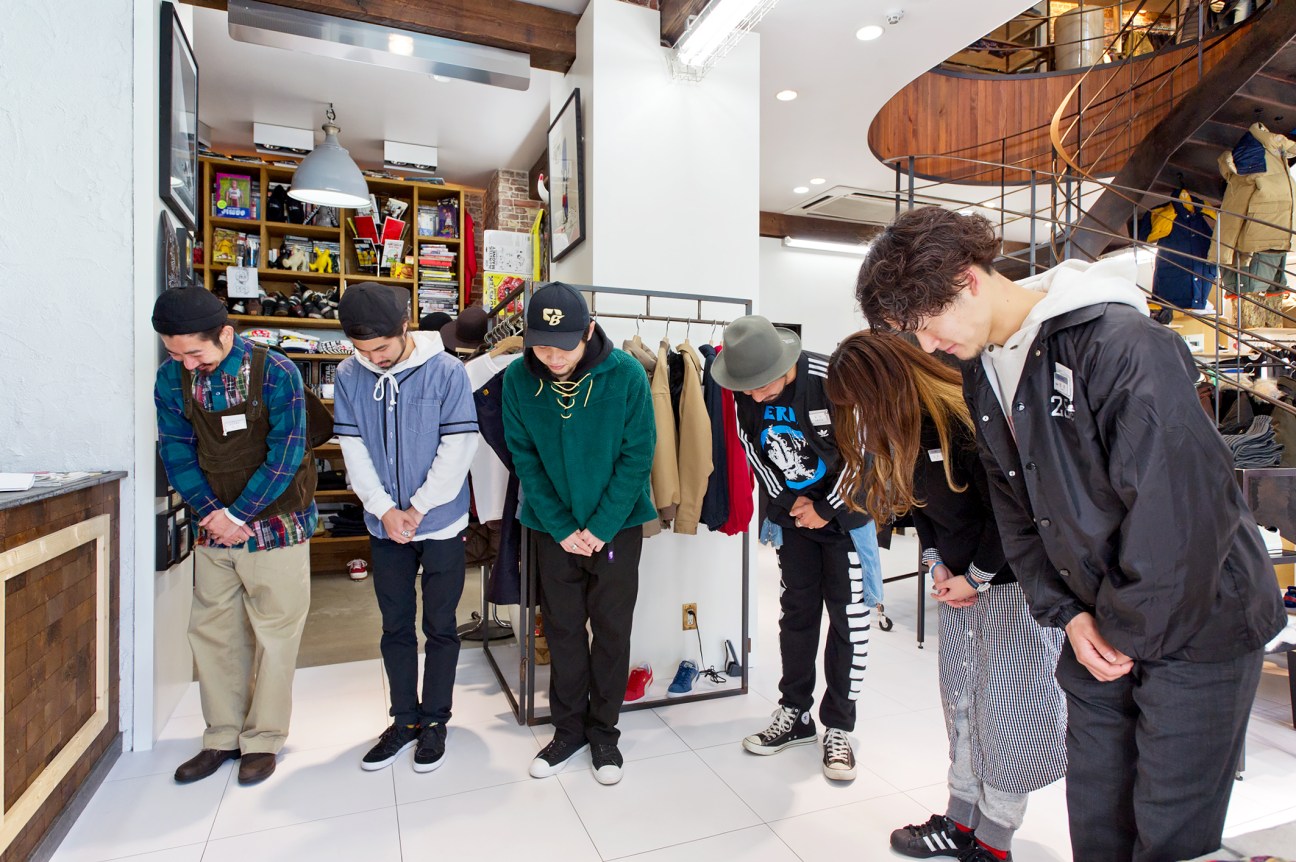 Beams staff members standing in a circle practicing bows during a morning meeting at the Harajuku shop.