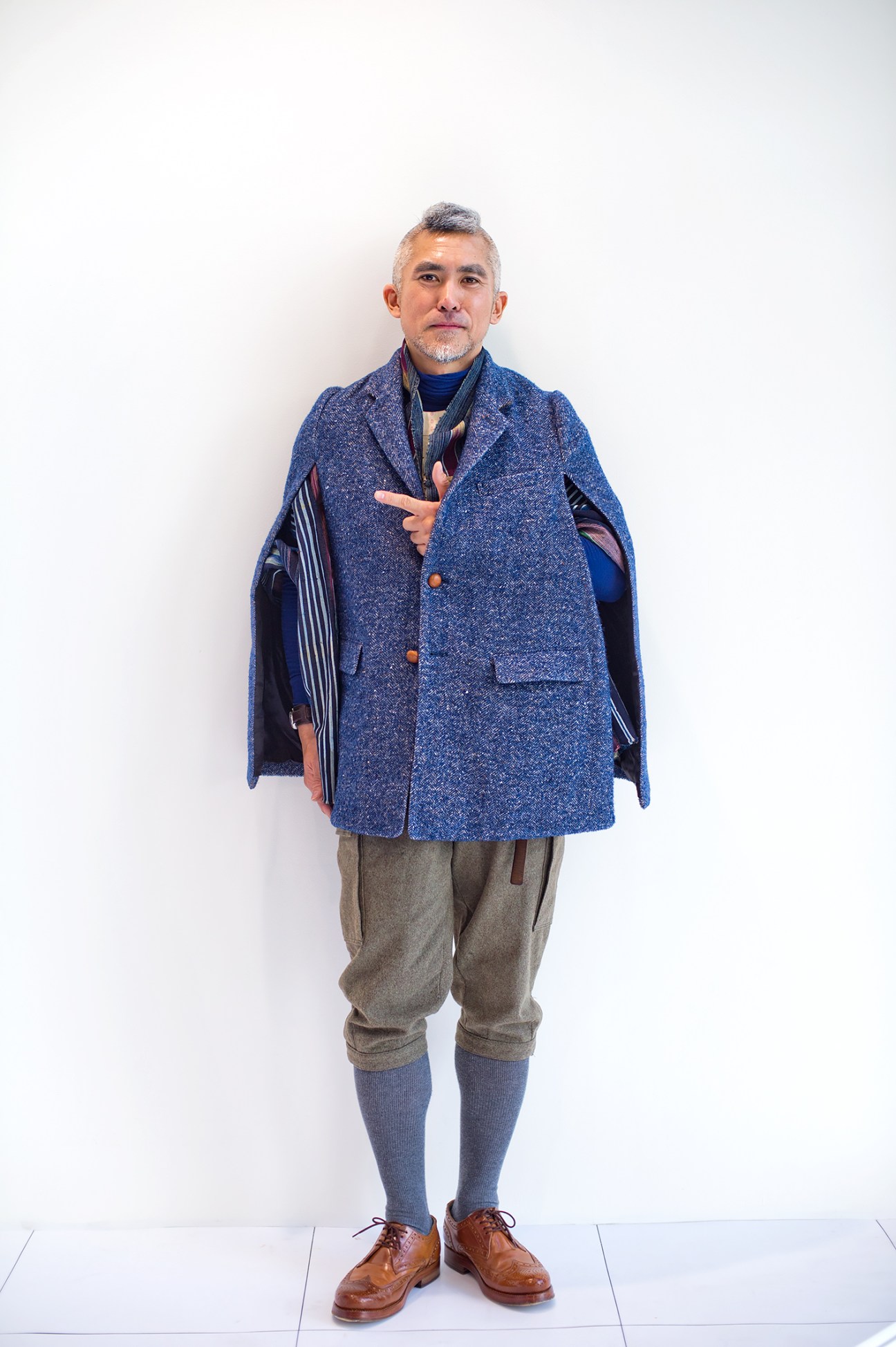 Kenjiro Wada wears a blue tweed cape, vintage knickerbockers, and brown leather brogues against a white background.