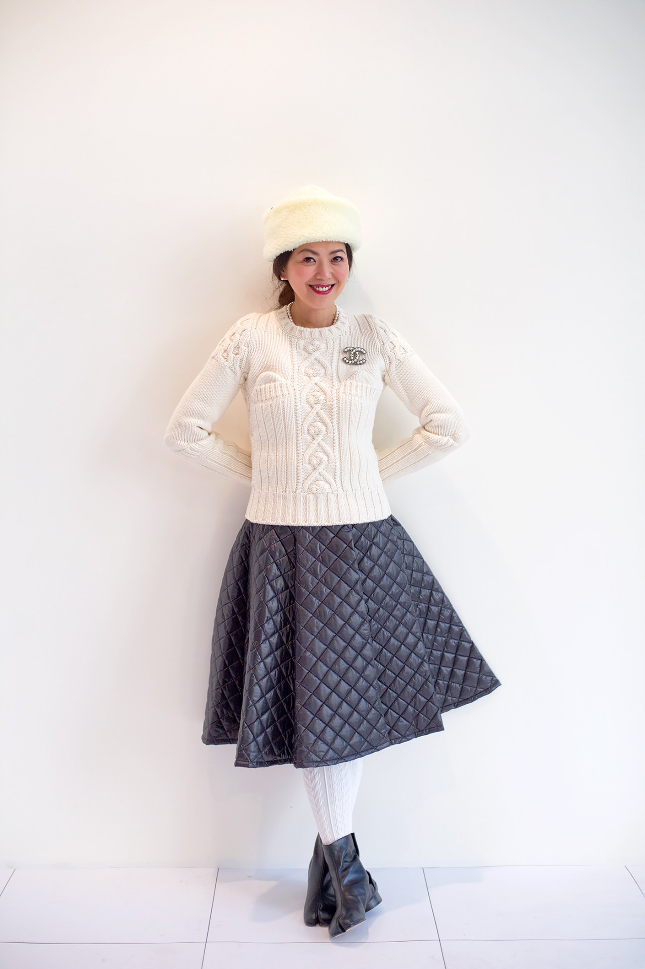 Mika Maruyama, styling director at Beams, poses in a cream cable-knit sweater, quilted skirt, white hat and black boots.