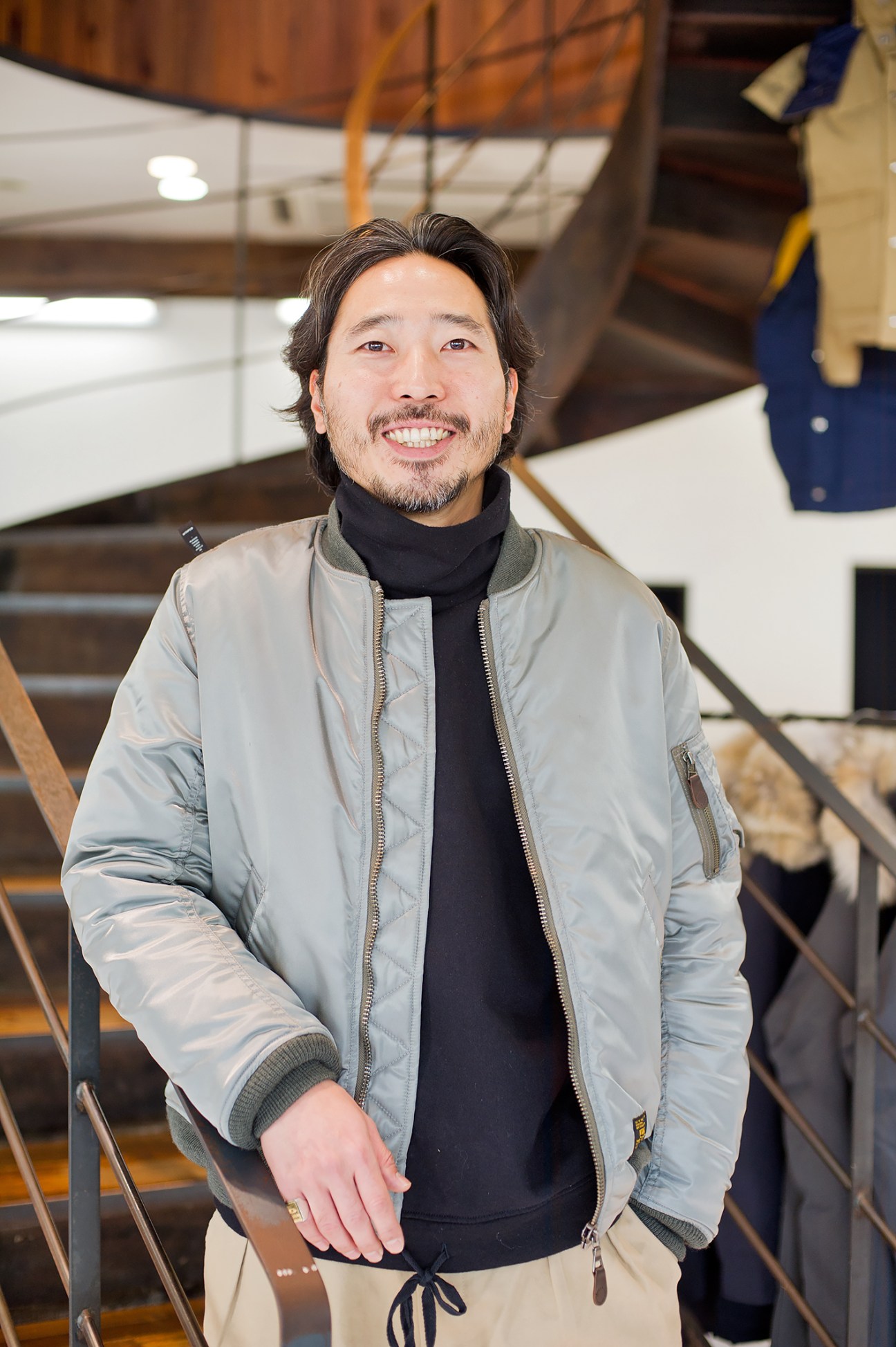 Takehiko Suzuki, Beams Harajuku shop manager, smiling in a light grey puffer jacket and black turtleneck.