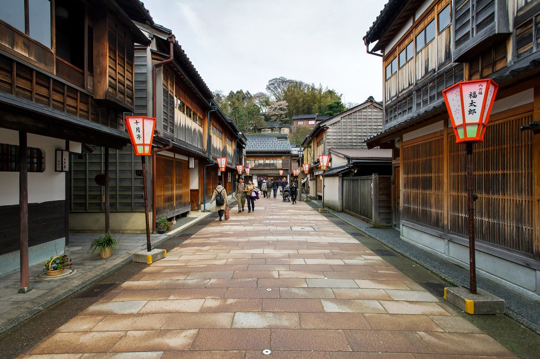 Traditional wooden machiya townhouses line a stone-paved street in Kanazawa's Higashi Chaya geisha district, with red lanterns hanging overhead.