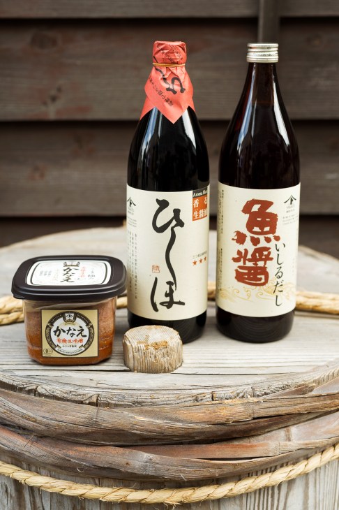 Yamato soy sauce and miso products displayed on wooden vessel with rustic background.