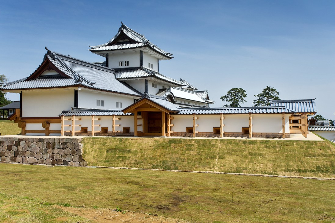 Kanazawa Castle with white walls, dark curved roofs, and stone fortifications under clear blue sky.
