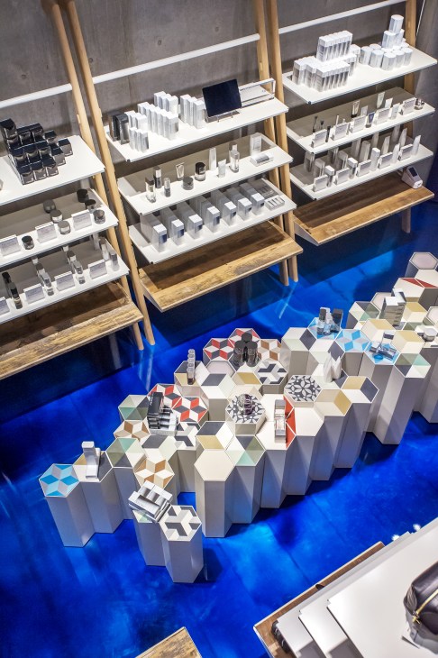 Overhead view of L'échoppe men's shop in Tokyo with white display shelves, wooden frames, and bright blue flooring.