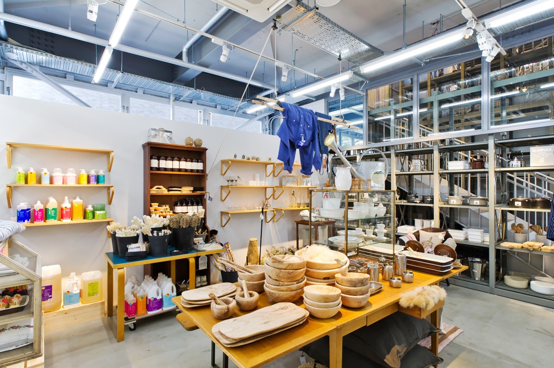 La Kagu shop interior displaying kitchenware, wooden bowls, dishes, and garden tools on yellow tables with shelving.