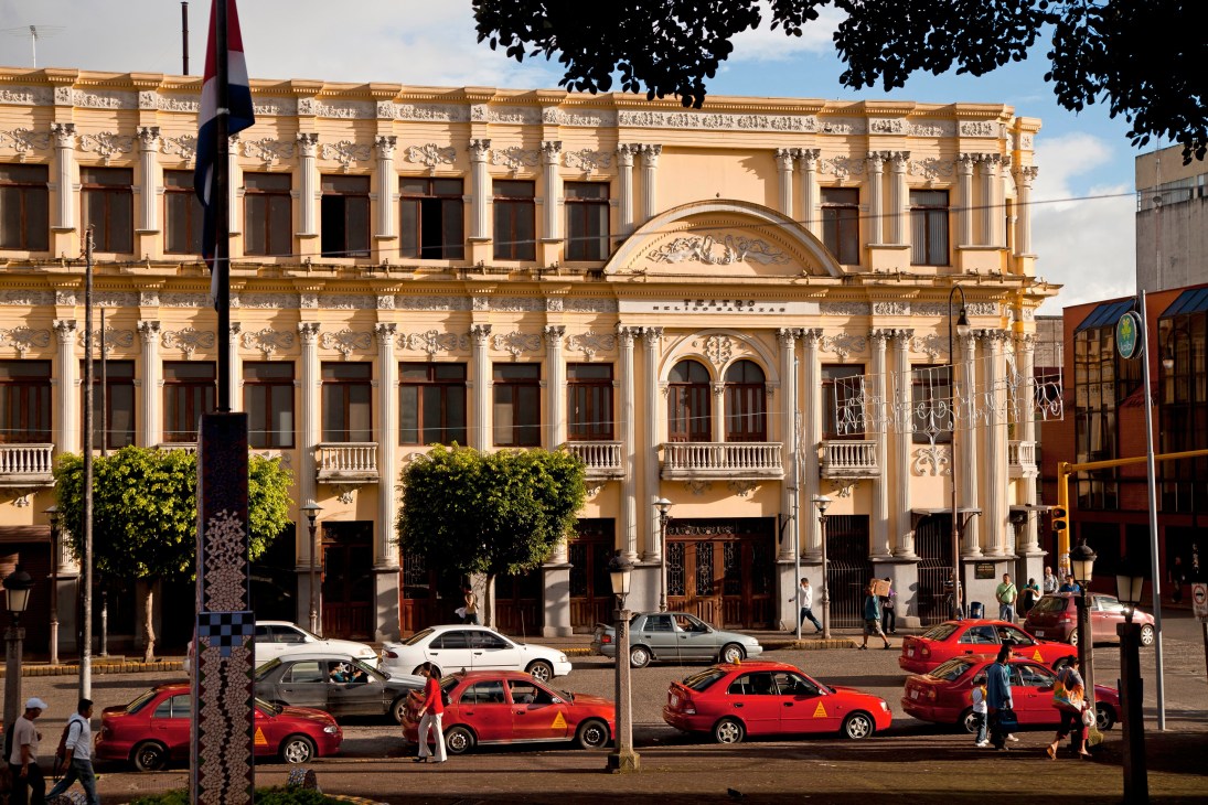 Melico Salazar Theatre, a neoclassical cream-colored building with ornate columns and arched windows, with red taxis parked in front.