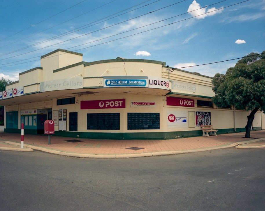 Curved corner building with cream and green exterior housing post office, liquor store and general merchandise in rural Australia.