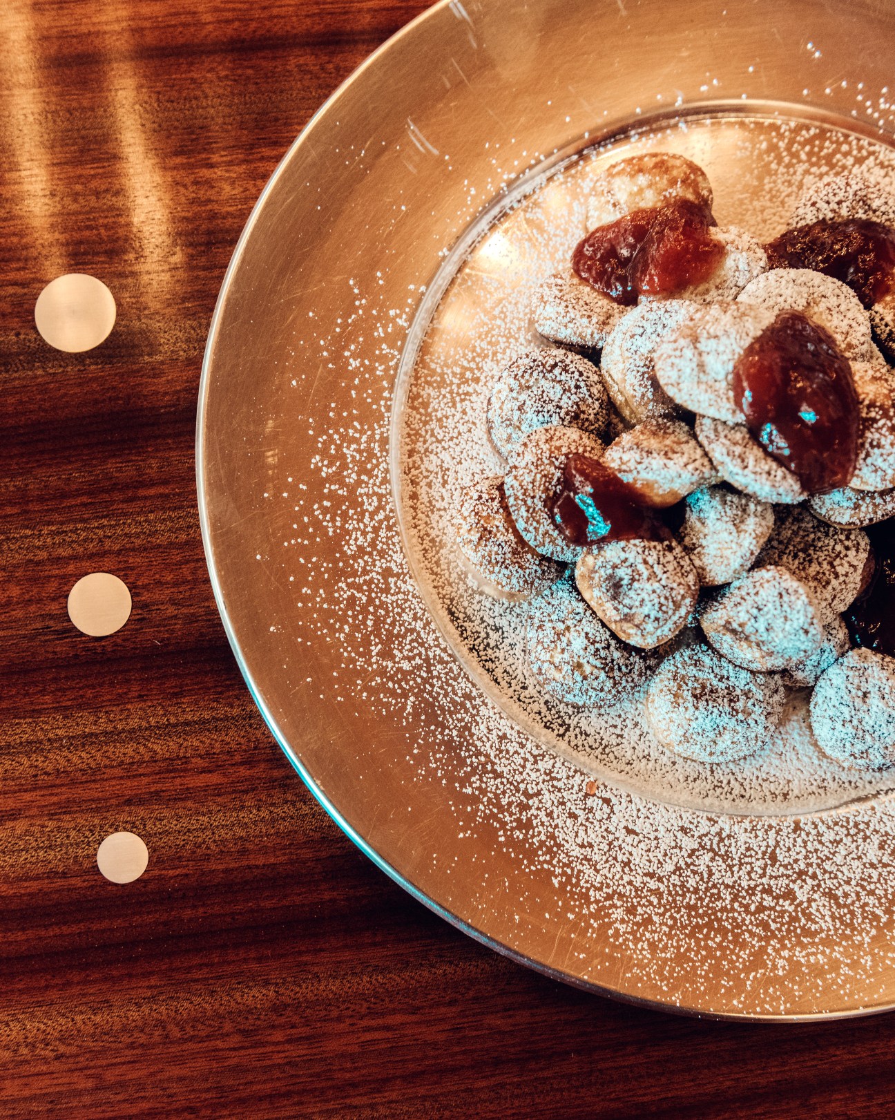 Powdered sugar-dusted aebleskiver apple puffed pancakes with red jam filling on a bronze plate.