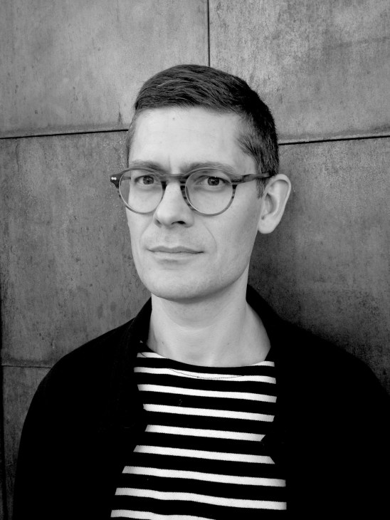 Black and white portrait of David Castenfors, editor in chief of Artlover magazine, wearing glasses and a striped shirt.