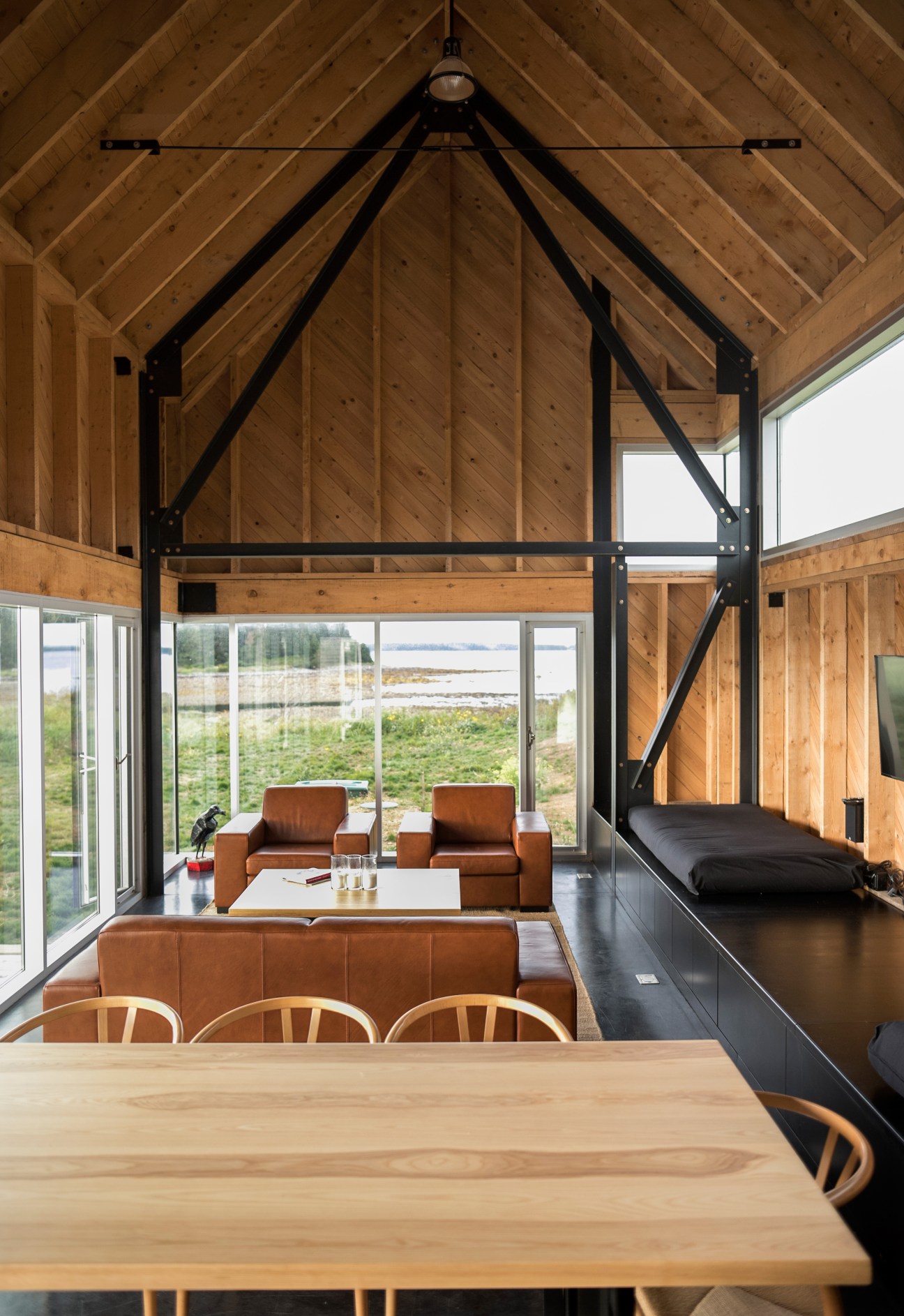 Modern wooden interior with exposed beams, leather seating, dining table, and large windows overlooking countryside
