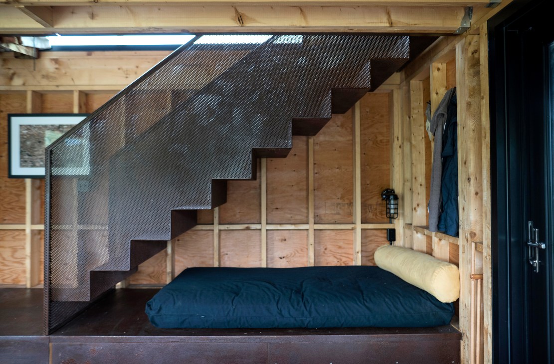 Blue futon mattress on wooden platform beneath industrial metal stairs with mesh safety barrier