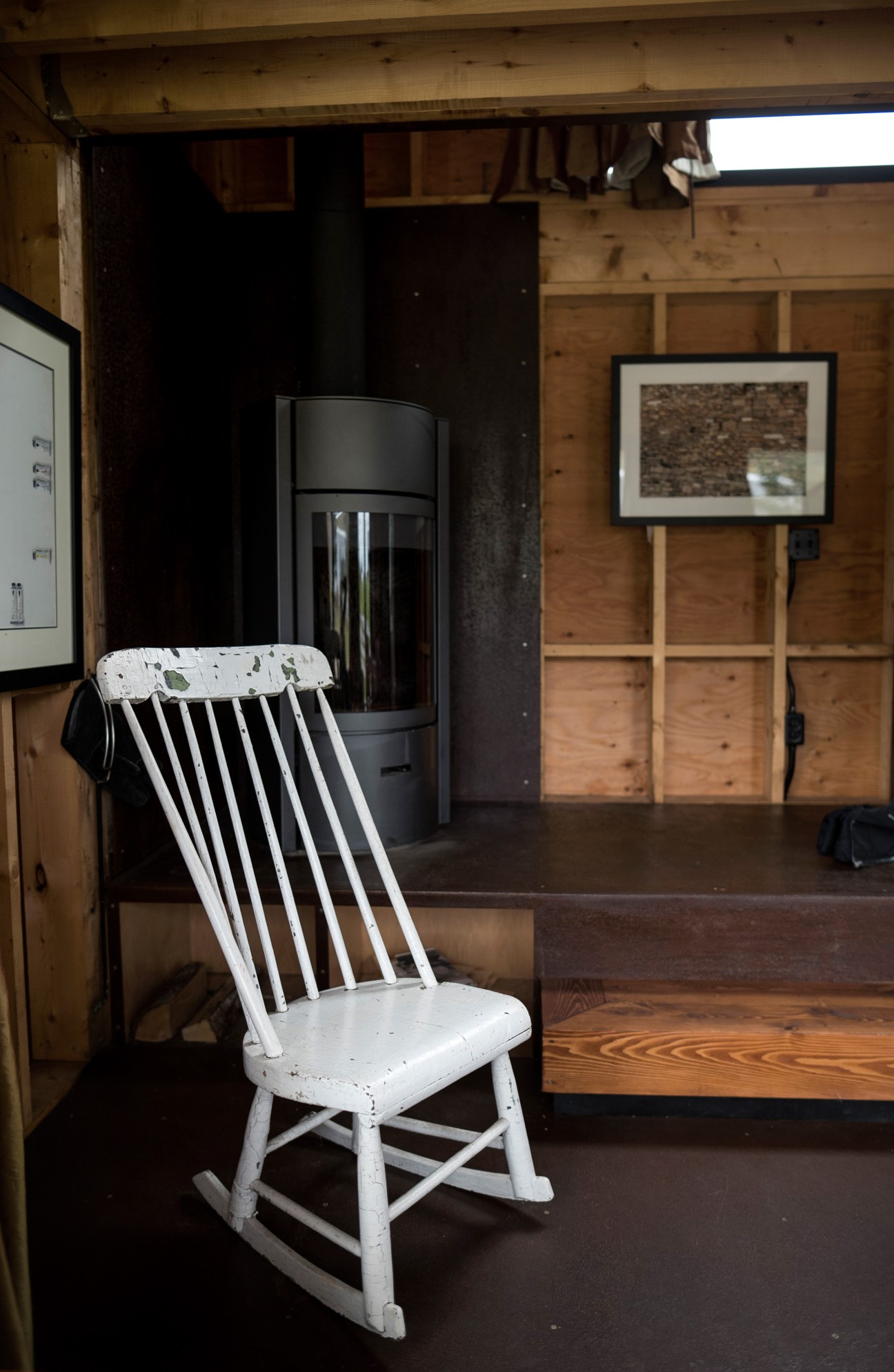 White Windsor-style rocking chair positioned near modern wood-burning stove in rustic cabin interior