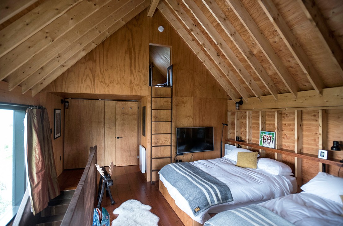 Wood-lined bedroom loft with exposed ceiling beams, twin beds, and ladder access in Enough House