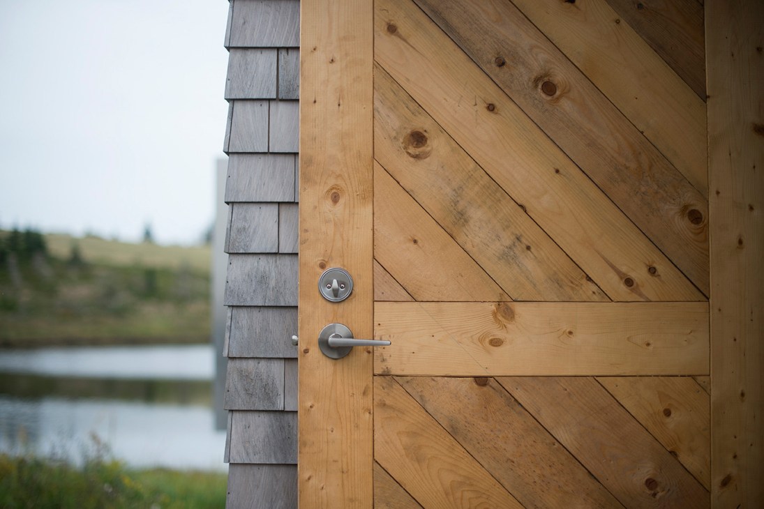 Natural wood door with diagonal planks and modern metal hardware on cedar-shingled building exterior