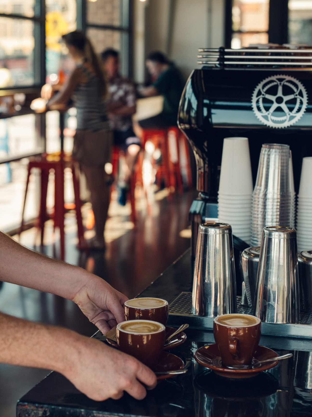 Barista serving latte art coffee cups at a Washington café counter with customers blurred in background.