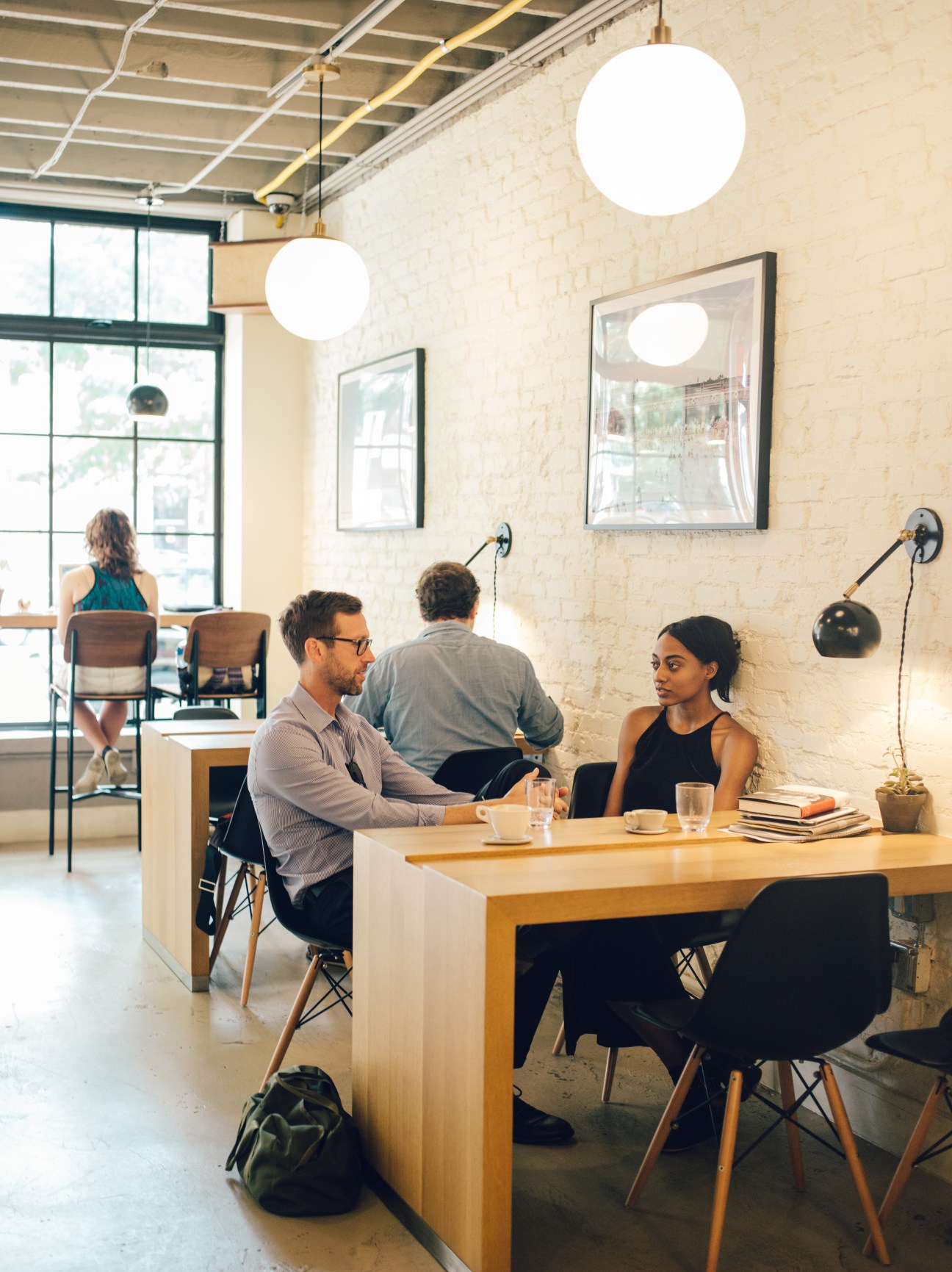 Modern café interior with customers at wooden counter, pendant lights, and exposed brick walls in Washington DC.