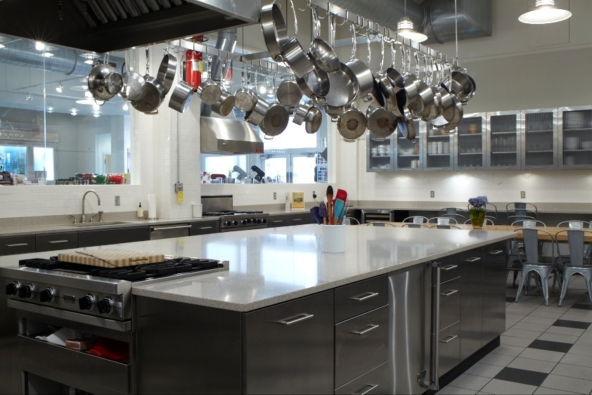 A modern professional kitchen with stainless steel cookware hanging above an island counter and Viking range.