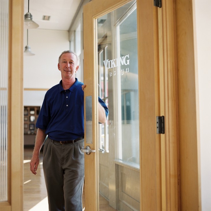 Bill Crump stands in a bright hallway next to a glass door marked 'Viking Design'.