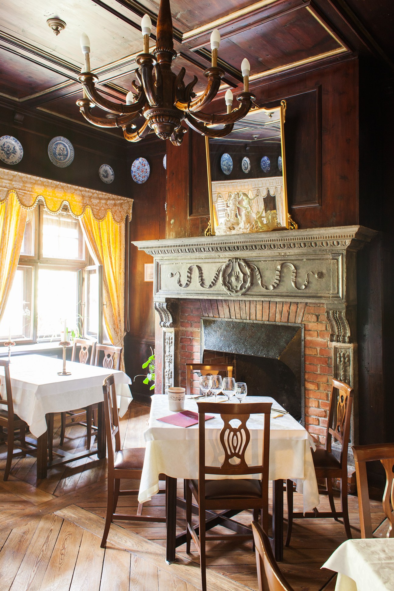 Elegant dining room with ornate wooden chandelier, Tuscan fireplace, and decorative plates displayed on dark walls.