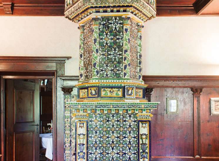 An ornate 17th-century Austrian furnace covered in colorful glazed majolica tiles featuring geometric and floral patterns, with a decorative crown-like top beneath a wooden ceiling.