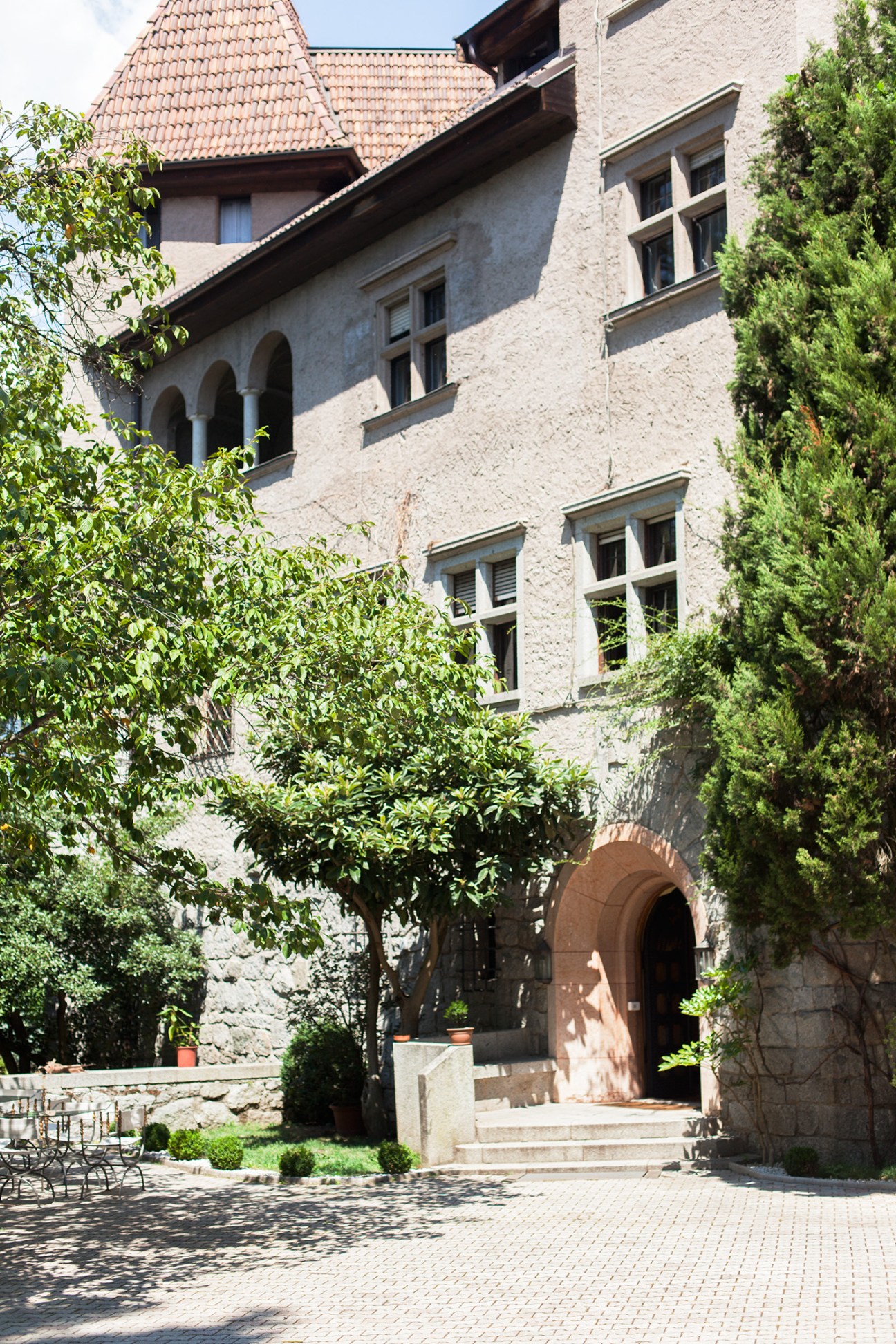Exterior facade of Castello Stifterhof with stone walls, arched windows, terracotta roof tiles, and ivy-covered courtyard entrance.
