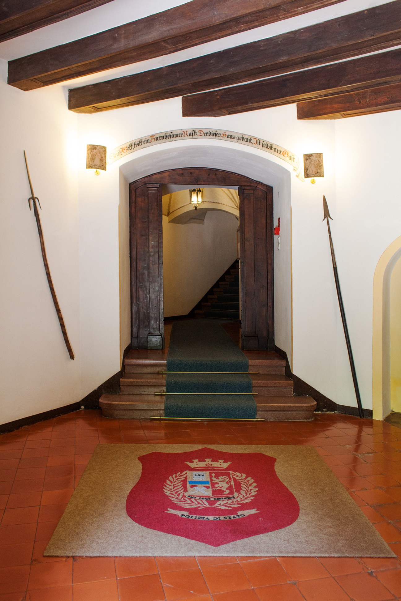 Castle entrance hallway with wooden beams, dark wooden door, and Polizia di Stato crest on floor mat.