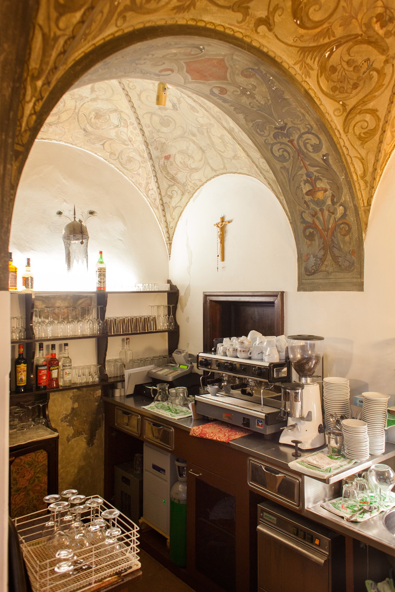 Bar counter beneath ornate vaulted arches with shelves of spirits and glassware.