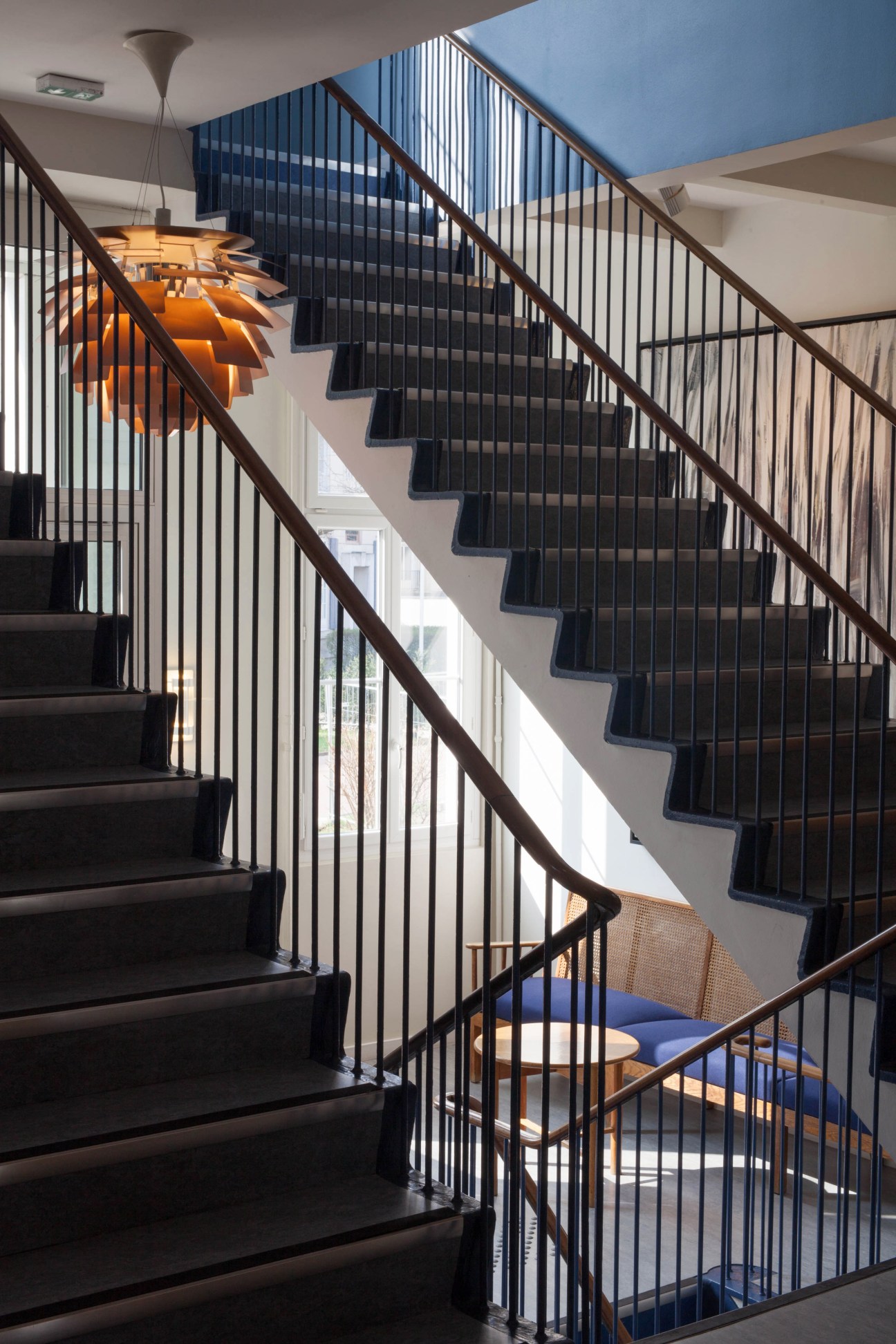 Modern staircase with black metal railings and wooden handrail, illuminated by an orange pendant light at the Fondation Danoise.