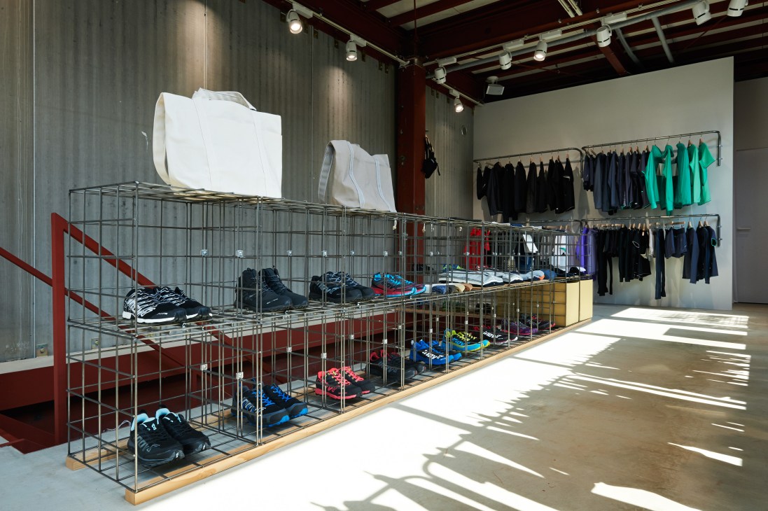Descente Blanc store interior with metal caged display fixtures holding shoes and clothing on adjustable bars.