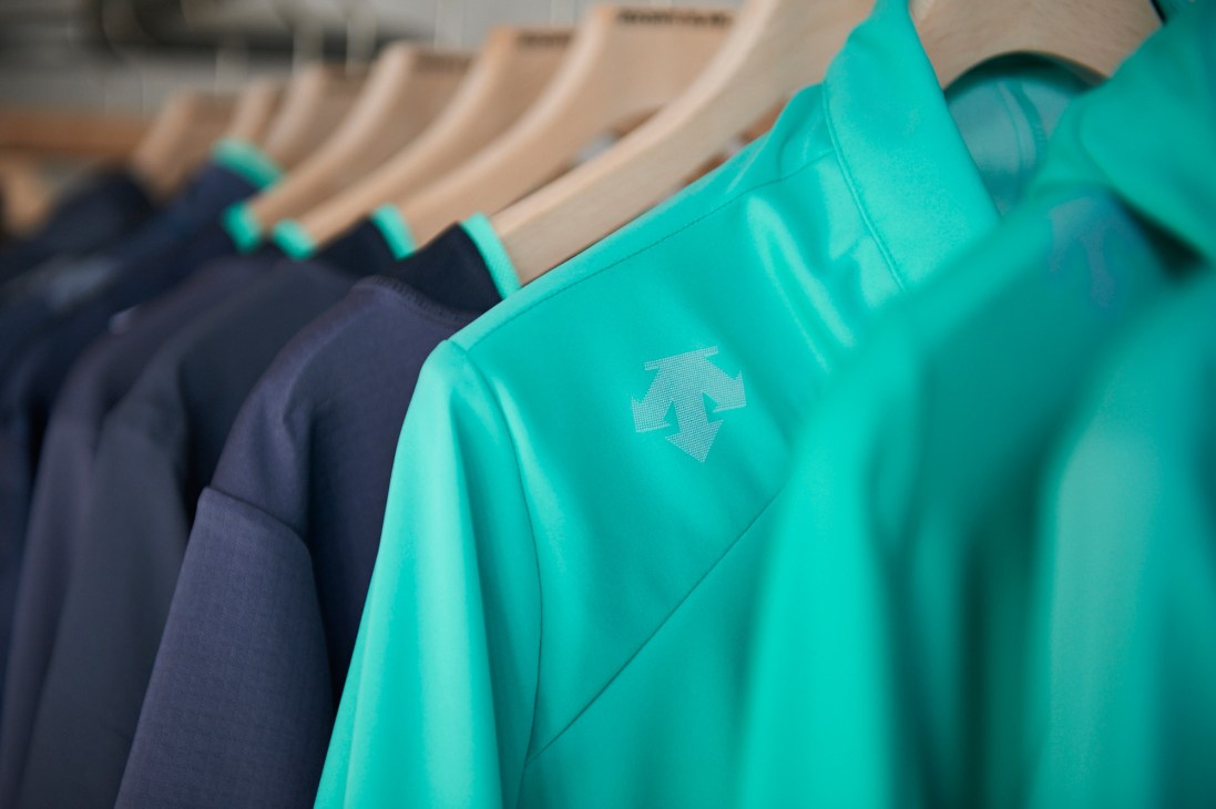 Turquoise and navy Descente Blanc jackets hanging on wooden hangers in a retail display.