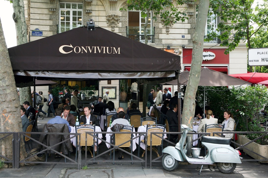 Convivium restaurant's street-level terrace in Paris's 16th arrondissement with diners seated under a black awning.