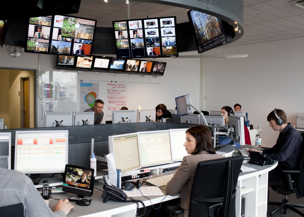 Deutsche Welle news desk with multiple editors and monitors displaying various broadcast feeds.