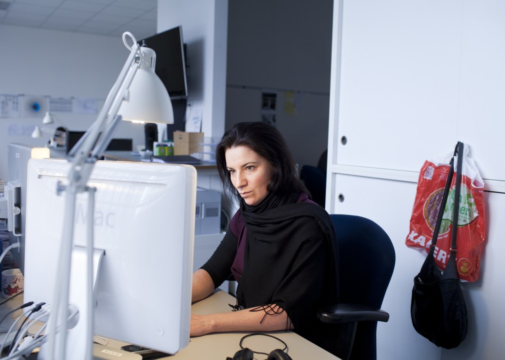 Woman working at a desk with a desk lamp and computer monitor in a modern office setting.
