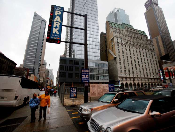 Urban street scene with parking sign, parked cars, pedestrians, and tall buildings in New York City.